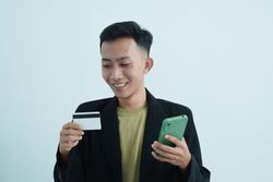 Smiling Asian businessman in suit holding blank credit card and smartphone