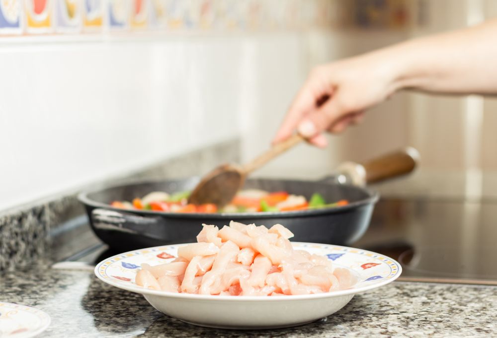 Raw chiken dish and female cooking in a pan