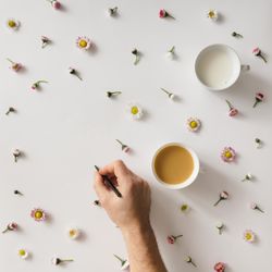 Hand holding pen with coffee and milk on light background with colorful flower pattern