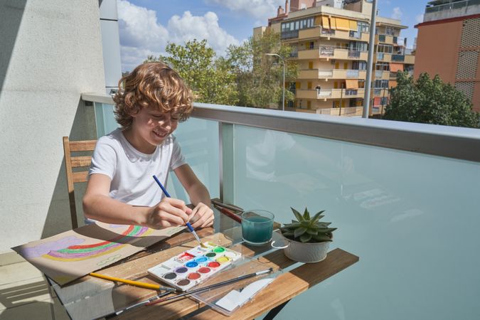 Content boy painting with watercolor on balcony of building