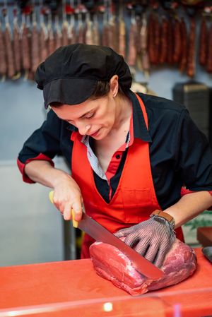 Butcher in apron cutting raw meat
