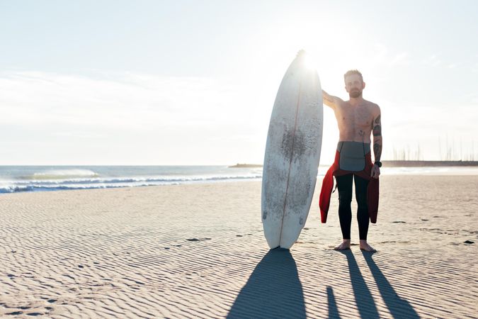 Portrait of surfer in the sun in wetsuit with surfboard, with copy space