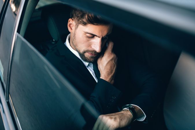 White business executive checking time and making phone call in car