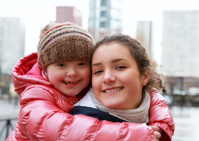 A young girl smiling on her teenager sister’s back on a cold day