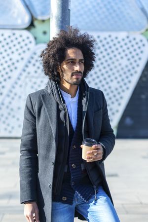Serious Black man in jacket with warm beverage standing outside