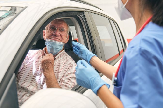 Crop physician with cotton bud against mature patient in auto