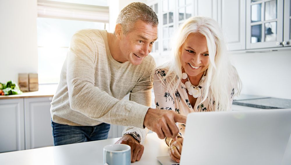 Mature couple smiling at something on a laptop screen in their kitchen