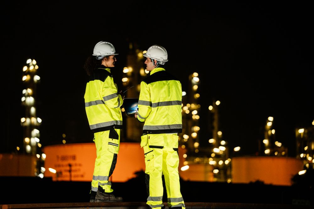 Back view of engineer worker discussing with colleagues, checking quality control at construction site of petroleum chemical industry or refinery oil plant factory overtime at night