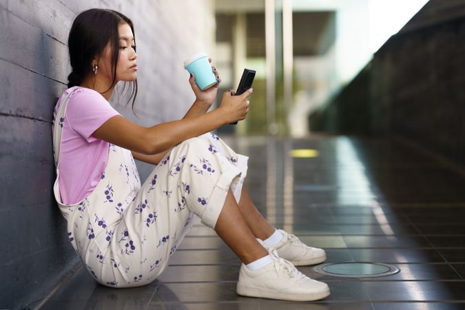 Serious female in floral overalls sitting on ramp checking her smartphone