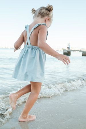Curious small girl having fun on sandy seashore near wavy sea