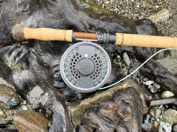 Fly fishing rod and reel on a piece of dark driftwood with riverbank