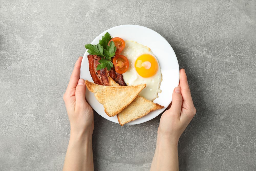 Hands reaching for breakfast plate on grey table
