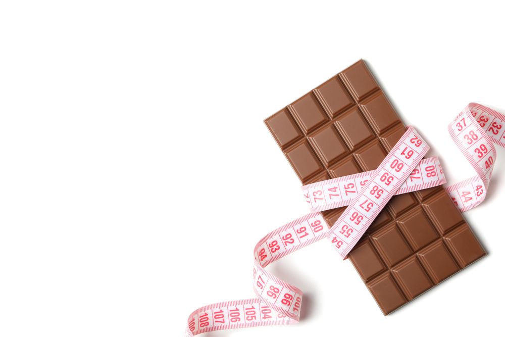 Measuring tape and chocolate bar on light background