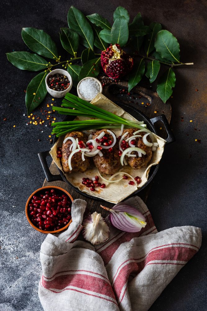 Looking down at Georgian plate of abkhazura meat cutlets with pomegranate seeds, bay leaves & onions