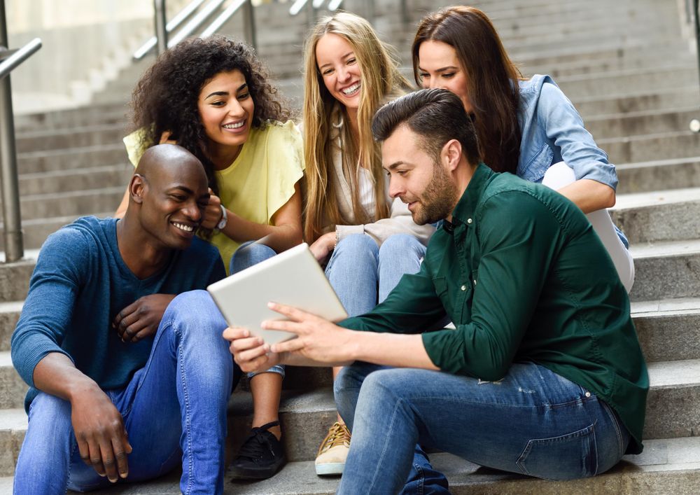 Men and women watching something on digital tablet while sitting on outdoor cement staircase