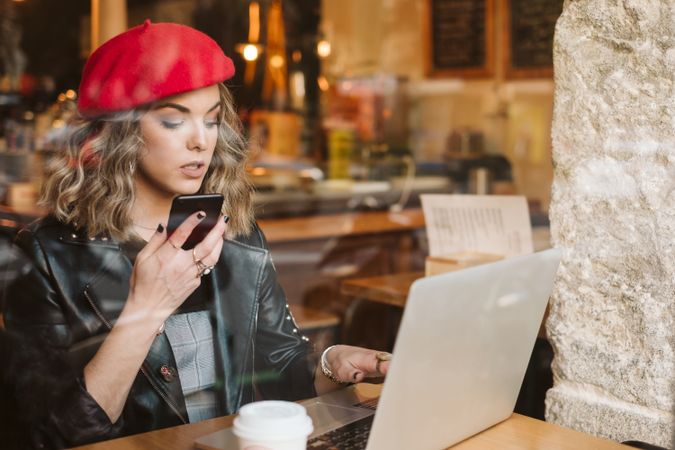 Woman with laptop using smartphone in cafe