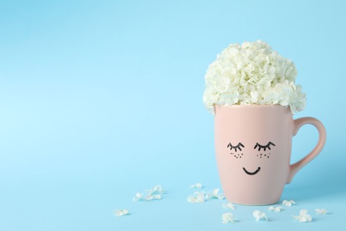 Cup with hydrangea flowers on blue background. Spring plant