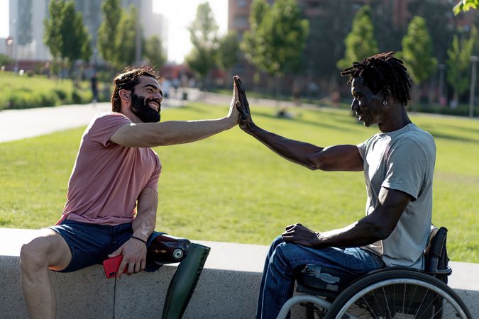 Two friends high-fiving, one in wheelchair and one with prosthetic leg
