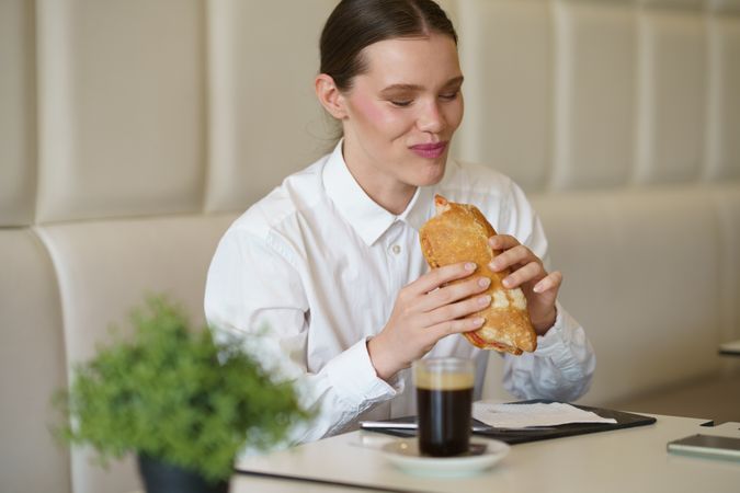 Smiling businesswoman eating a sandwich in a modern coffee shop