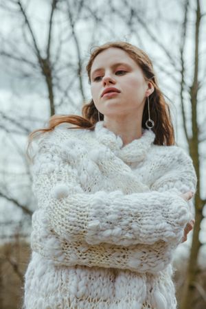 Woman in light dress and wool jacket standing near bare trees