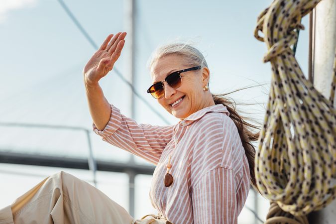 Stylish older woman sitting on a yacht bow waving