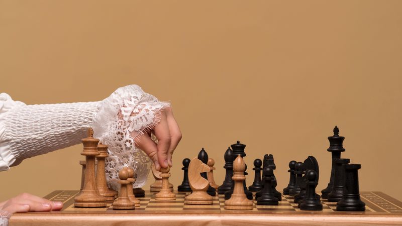 Hand in lace sleeve adjusting chess piece during game.