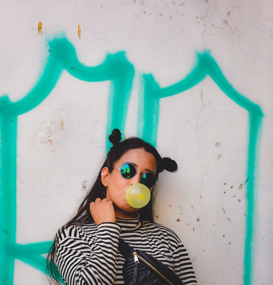 Woman blowing bubble gum standing beside wall
