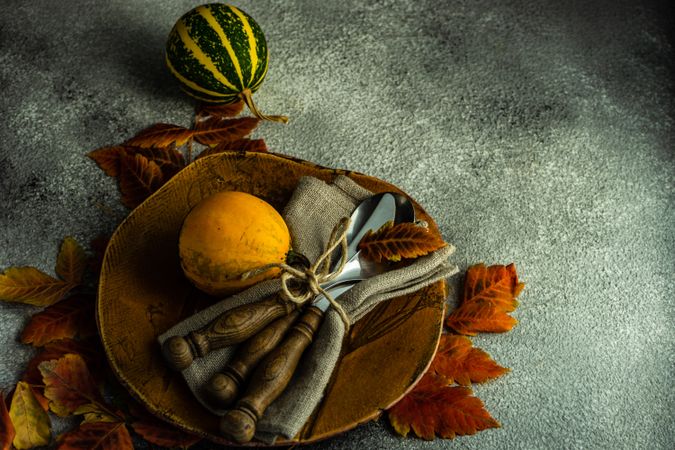Ceramic brown plate in autumnal table setting with gourds and leaves