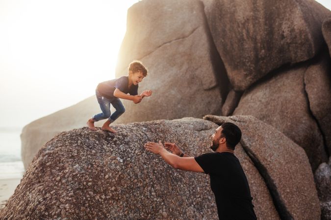 Happy little boy jumping into his father's arms from a rock