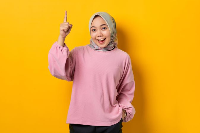 Smiling Muslim woman smiling and pointing upwards with good idea