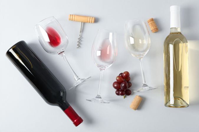 Flat lay. Grapes, corkscrew, bottles and glasses with wine on grey background