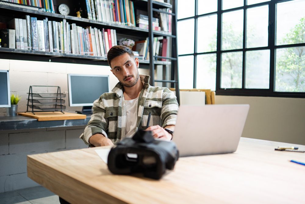 Serious young designer sitting at desk with VR headset