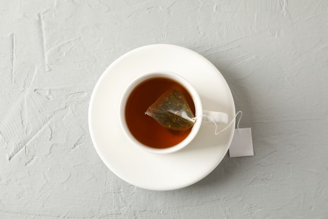 Cup of tea with tea bag on grey background, top view