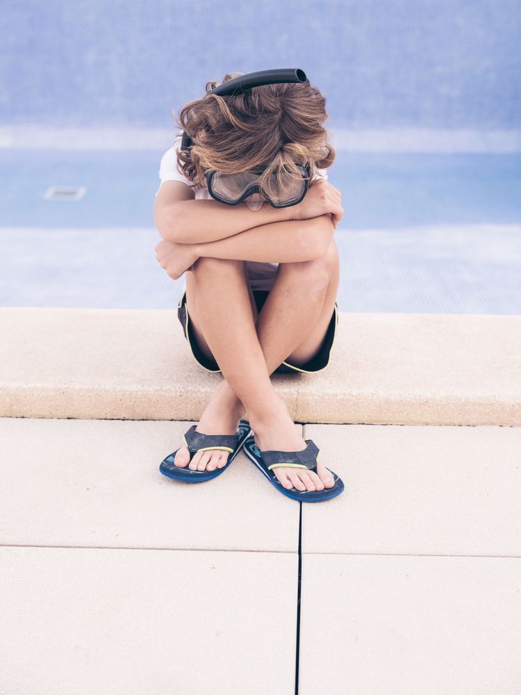 Frustrated kid in swimming glasses on pool border