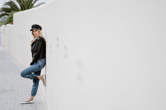 Stylish woman confidently leaning on white wall