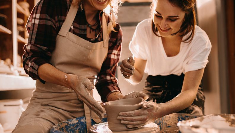 Two women at a pottery workshop making clay pots in artist's studio