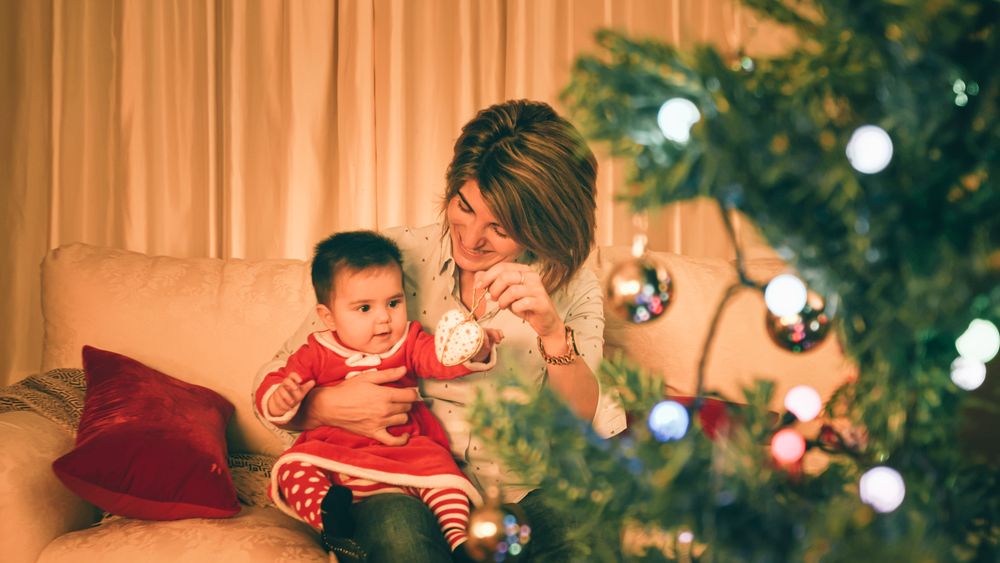 Mother playing with baby near Christmas tree
