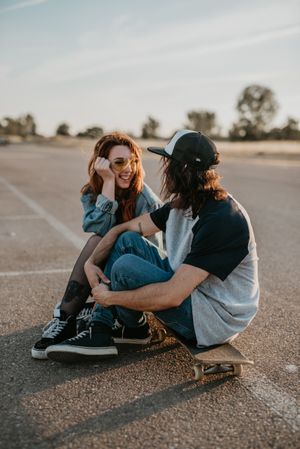 Skaters sitting on empty rural road chatting in sunlight