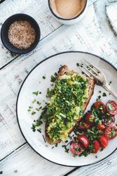 Avocado toast on sourdough bread, cherry tomatoes and coffee, on light background, top view