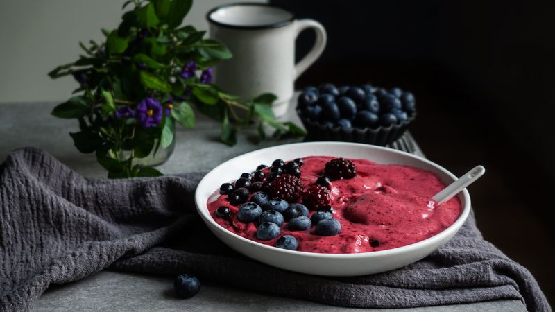 Smoothy of fresh bog blueberries and raspberries in bowl near napkin