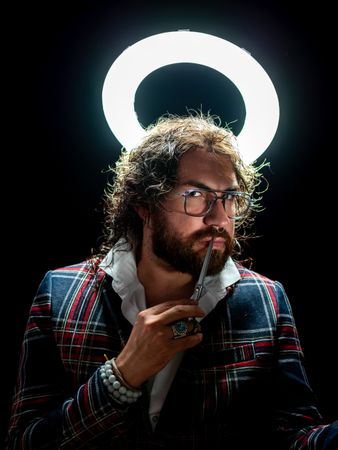 Serious man with glowing fake nimbus holding mirror and looking at camera