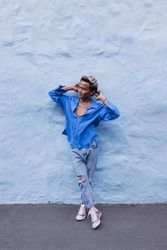 Man in a blue shirt leaning wall outdoors while running his hands through hair, vertical