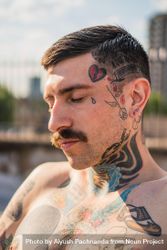 Shirtless white hipster man with mustache closing eyes in sunlight with face and neck tattoos 4Od2vb