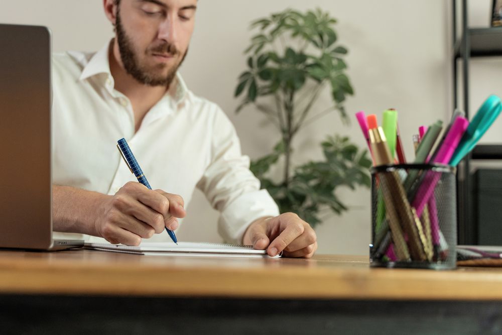 Close up of a man writing in a notebook at his desk.