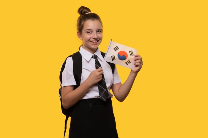 Smiling schoolgirl holds South Korean flag while posing.