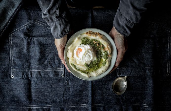 Person holding bowl with cauliflower puree with pesto and eggs