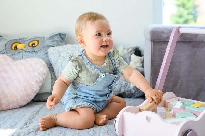 Happy little baby playing with blocks in cart in bedroom