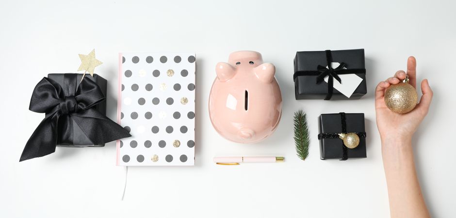 Piggy bank, balls, gift boxes and female hand on light background, top view