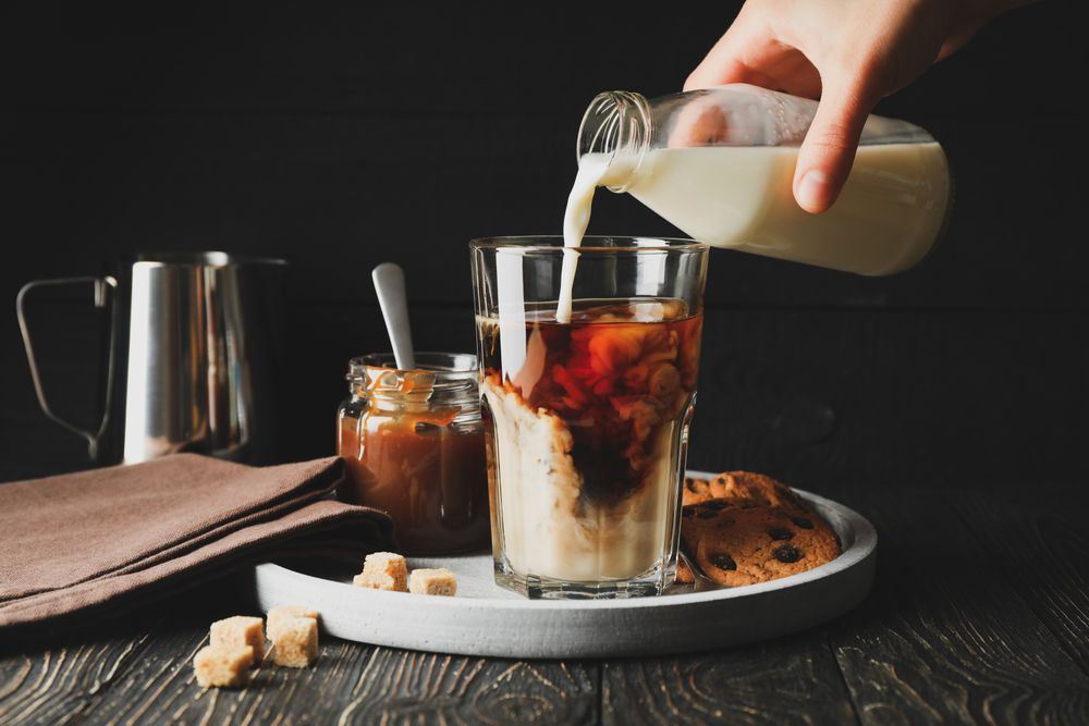 Woman pours a milk in glass of coffee. Composition with ice coffee