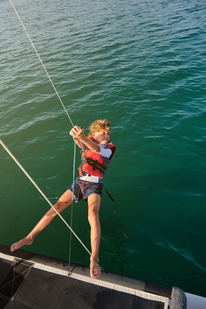 Preteen kid tightening ropes on sails of boat